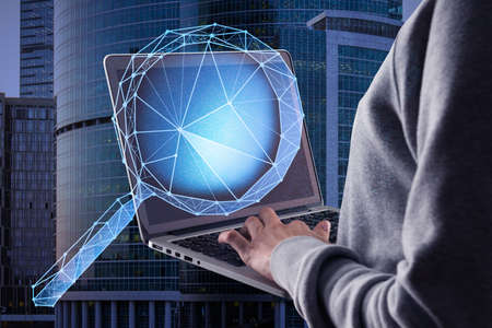 Close up of hacker hand using laptop with abstract polygonal magnifying glass on blurry city...