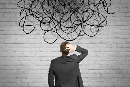 Back view of businessman looking at abstract scribble on brick wall background. Question, think and...