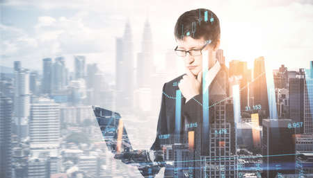 Portrait of handsome young european businessman using tablet on bright city background with mock up place and candlestick forex chart. Technology, trade, finance, communication and success concept. double exposureの写真素材