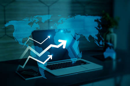 Close up of office desktop with laptop computer and abstract glowing growing business arrow and map hologram on blue background. Technology and internet data concept. double exposureの写真素材
