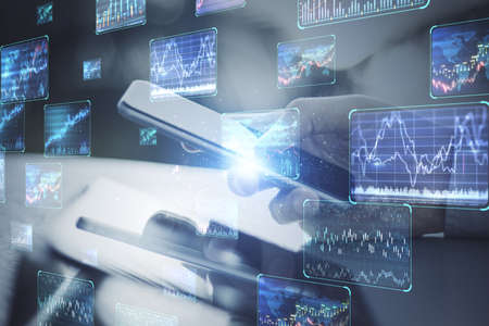 Close up of hand at desktop using smartphone with various forex screens on blurry background....