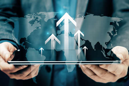 Close up of businessman hand holding tablet with abstract glowing growing business arrow and map hologram on blue background. technology and internet data conceptの写真素材