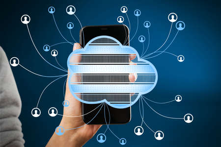 Close up of hand holding smartphone with abstract cloud computing hologram on blurry blue background. Technology, database, communication and connection concept. double exposureの写真素材