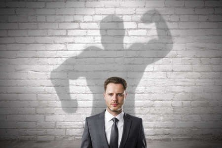Abstract image of attractive european businessman with strong muscle shadow on brick wall background. Confidence and strength conceptの写真素材