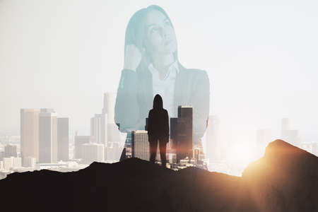 Thoughtful businesswoman on mountain top. Leadership and future concept. Abstract city background with sunlight and silhouette. double exposureの写真素材