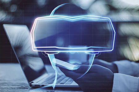 Close up of businessman hands using laptop with abstract hologram of digital head with VR glasses on...