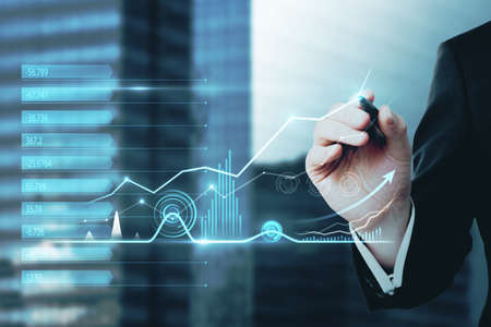 Close up of hand with pen pointing at abstract business chart hologram on blurry city background. Dashboard, investor and finance concept. double exposureの写真素材