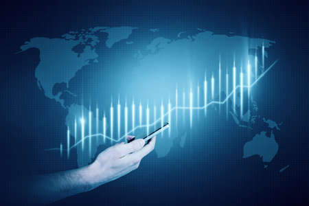 Close up of male hand holding smartphone with glowing blue business chart hologram with map on...