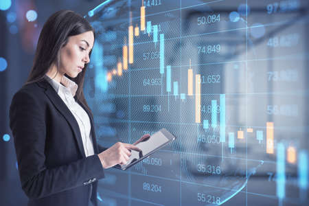 Attractive worried young businesswoman using tablet while standing in blurry office interior with...