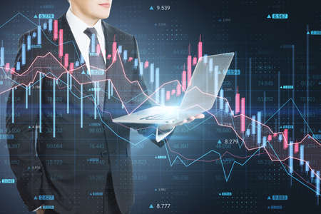 Businessman hand using laptop with abstract downward forex chart on blurry dark background. Crisis,...