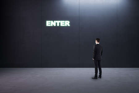 Thoughtful young businessman standing in concrete interior with entrance to success. Way and...