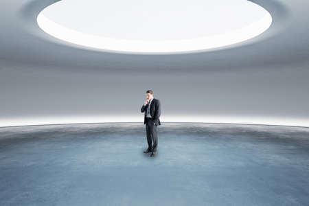 Thoughtful young european businessman standing in abstract space ship interior with spotlight from...