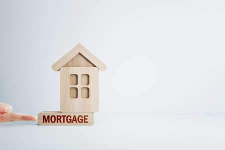 Finger pushing abstract wooden house on white mortgage background with mock up place. Loan, bank and money conceptの写真素材