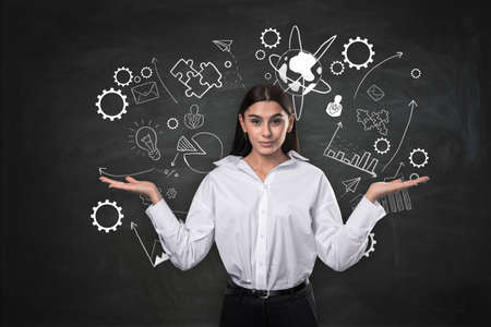 Attractive confused young european businesswoman with abstract business, science and education sketch on chalkboard wall background. Workshop and career conceptの写真素材