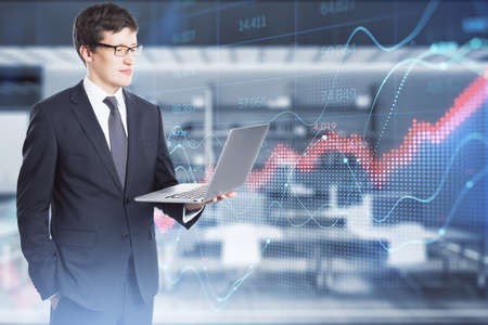 Attractive young white businessman using laptop with abstract red forex chart index on blurry office...