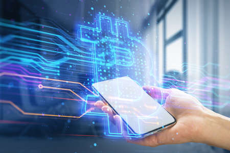 Close up of female hand holding smartphone with creative blue bitcoin hologram on blurry office...