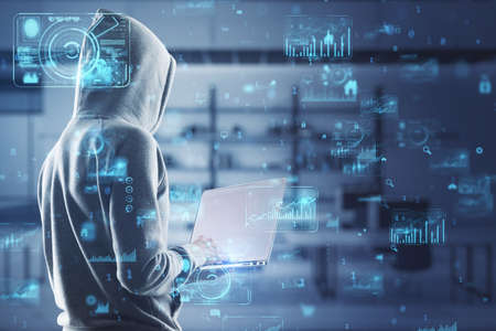 Hacker in hoodie using laptop with abstract creative business charts and binary code on blurry...