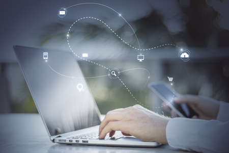 Close up of hand using laptop keyboard and smartphone with abstract SEO search and communication hologram on blurry background. double exposureの写真素材