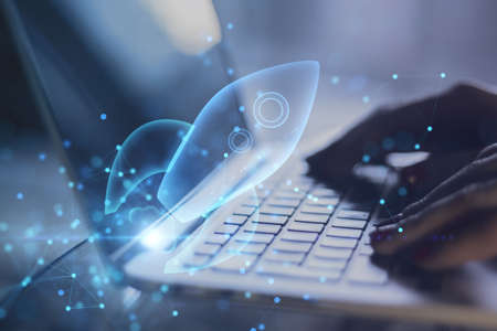 Close up of backlit hands using laptop with abstract glowing blue rocket space ship on blurry background. Startup and company growth concept. double exposureの写真素材