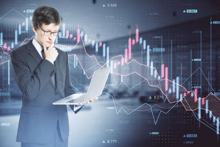 Businessman hand using laptop computer with abstract downward forex chart on blurry dark background....