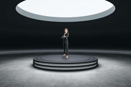 Thoughtful young european businesswoman standing in abstract space ship interior on round pedestal with spotlight from above. presentation conceptの写真素材