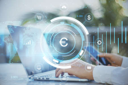 Close up of businessman hands using laptop and smartphone with creative glowing round euro chart...