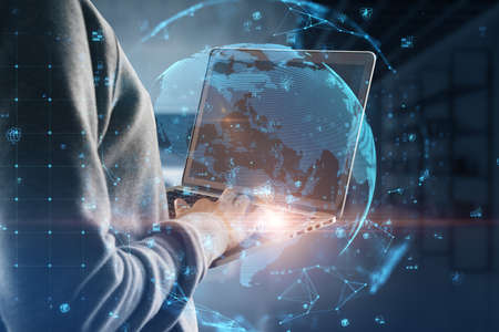 Close up of hand using laptop with glowing polygonal globe with social icons on blurry office interior background. Connect and data concept. double exposureの写真素材
