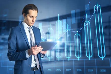 Attractive young european businessman using tablet with growing annual business chart report...
