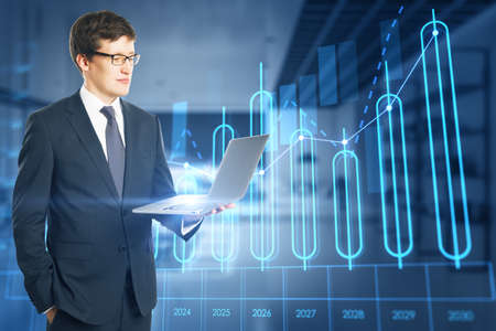 Attractive young european businessman using laptop with growing annual business chart report...