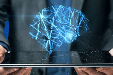 Close up of businessman hands holding tablet with abstract shiny blue digital brain hologram on dark background. Human technology, research and science conceptの写真素材