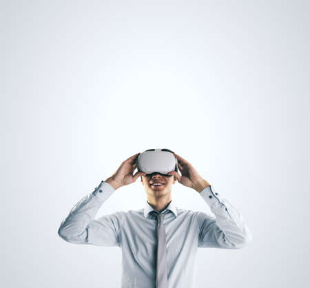 Virtual reality concept with young businessman gets new emotions in VR glasses on abstract light gray background and empty space on his head for you text, mock upの写真素材