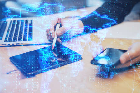 Close up of hands using digital tablet with pen and smartphone with glowing blue map hologram and...