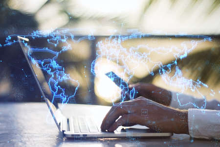 Close up of hands using laptop and smartphone with glowing blue map hologram and digital data...