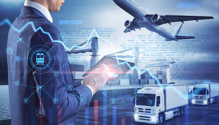 Close up of businessman hand holding tablet or smartphone with abstract glowing shipping hologram on dock with transport background. Export, logistics and freight concept. double exposureの写真素材