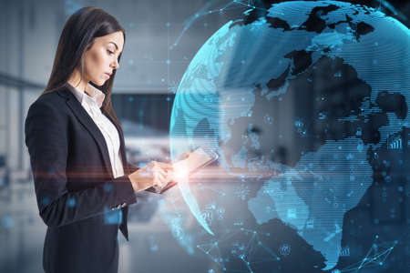 Attractive young caucasian businesswoman using tablet with glowing polygonal globe and social icons...