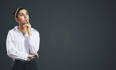 Thinking concept with pensive businesswoman in white shirt and dark trousers standing on abstract black wall backdrop, with empty place for you text, mock upの写真素材