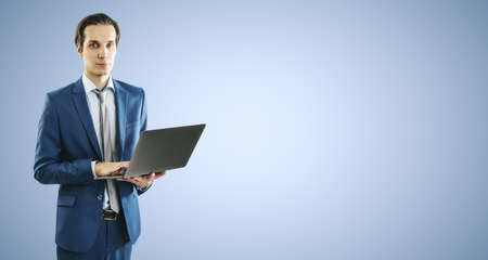 Young businessman in blue suit working with modern laptop, isolated on light blue wall background, with blank place for you text or logo, mockupの写真素材