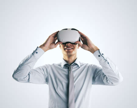 Virtual reality concept with young businessman gets new emotions in VR glasses on his head on abstract light gray background, close up, isolatedの写真素材