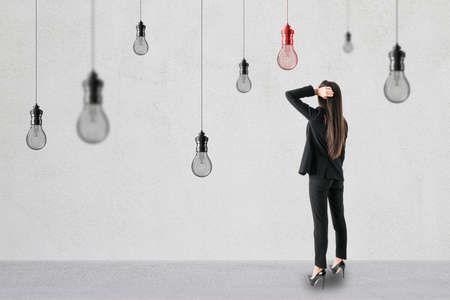 Side view of thoughtful attractive young european businesswoman standing in simple concrete interior with many hanging light bulbs. Idea, success and worker conceptの写真素材
