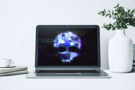 Close up of laptop computer screen on desktop with abstract digital skull hologram. Hacking,...