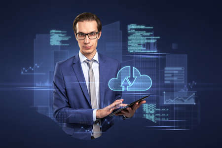 Attractive young european businessman with tablet standing on abstract blue background with coding...