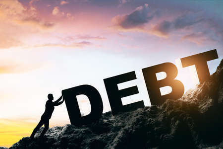 Consumer debt high burden crisis and financial concept with man trying to get up big sign debt on the rock at sunset backgroundの写真素材
