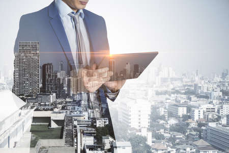 Headless young european businessman with tablet standing on abstract bright city background with mock up place. Success, technology, communication and employment concept. double exposureの写真素材