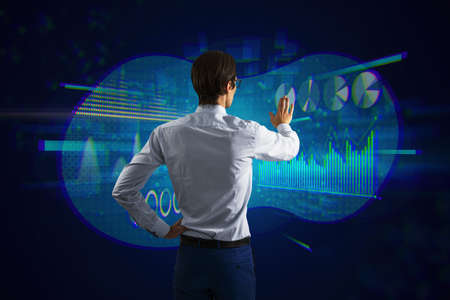 Back view of attractive young european businessman using abstract glowing digital business chart and...