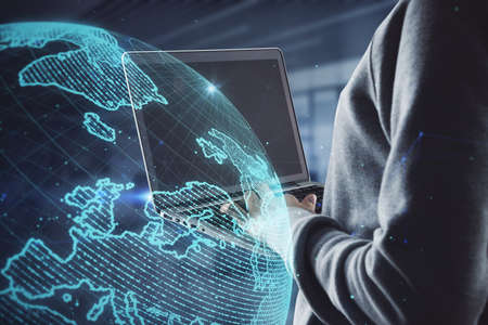 Close up of hacker hands using laptop computer with creative glowing polygonal grid planet on blurry...