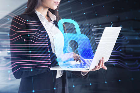 Young european businesswoman using laptop with glowing padlock hologram and lines on blurry office...
