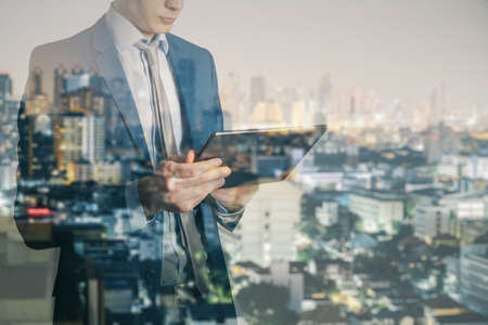 Headless young businessman using tablet on blurry illuminated night city background. Technology and communication concept. double exposureの写真素材