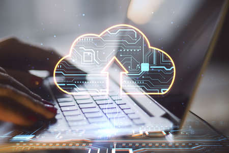 Close up of female hands using laptop keyboard with glowing circuit cloud hologram on blurry background. Cloud computing and database conceptsの写真素材