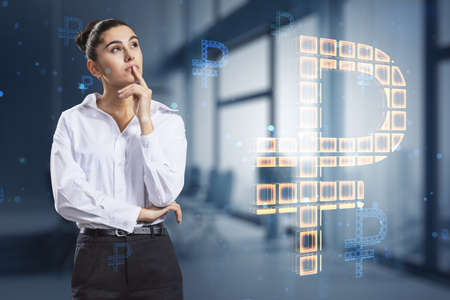 Attractive thoughtful young european businesswoman with creative glowing Russian ruble hologram on blurry office interior background. Digital money and online banking concept. double exposureの写真素材