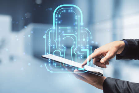Close up of businessman hand pointing at pad with glowing padlock hologram on blurry office interior...